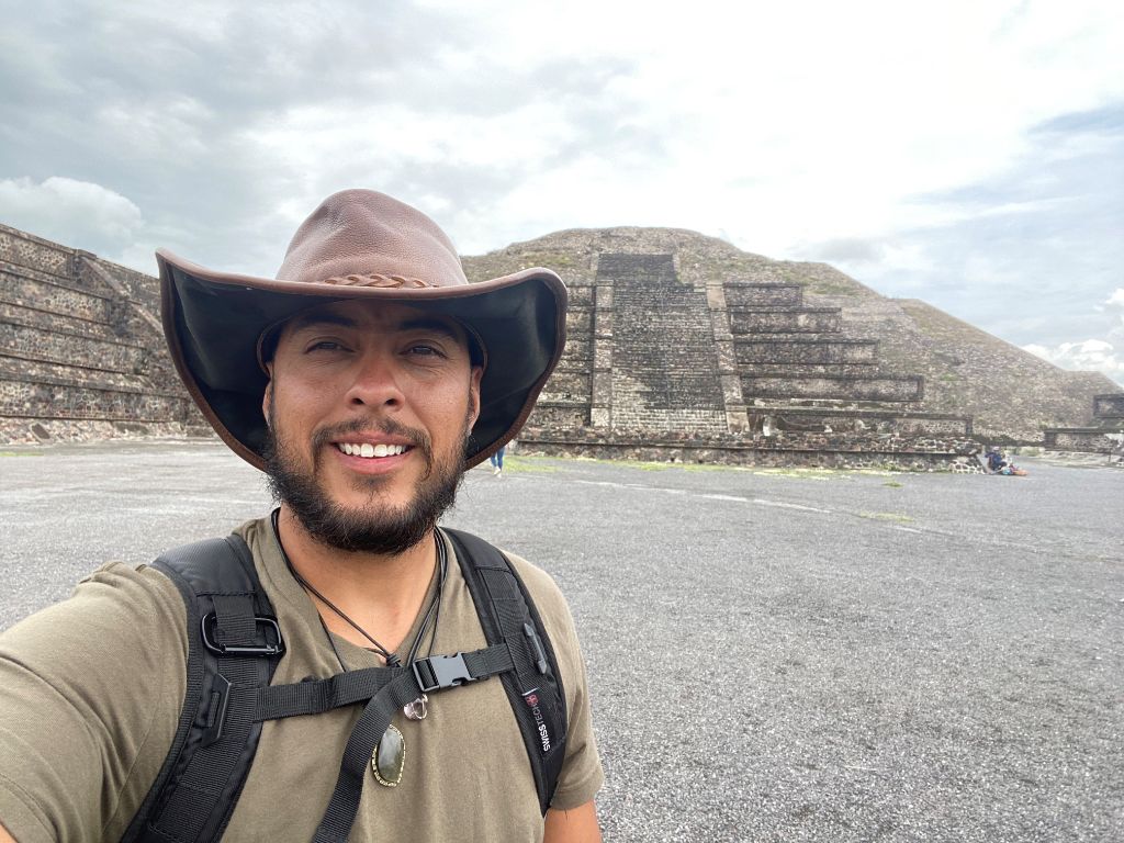 Selfie of Alex wearing a leather cowboy hat and lightly smiling in front of an ancient pyramid with spiritual significance.