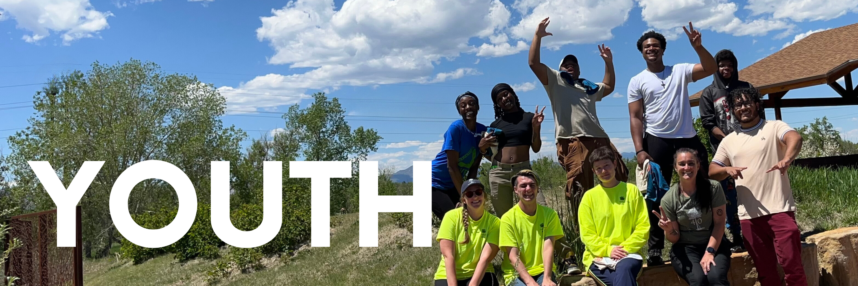 Youth. Image of a group of youth smiling with arms around each other. Mountains and a blue sky are in the background.