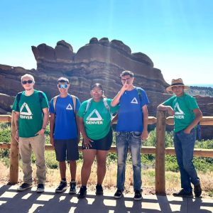 5 members of the Green Team smile into the camera. They're in front of a large redrock formation.