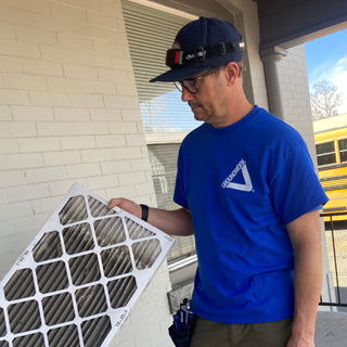 Energy auditor in a blue Groundwork Denver shirt looks down at a very dirty home air filter that he's replacing.